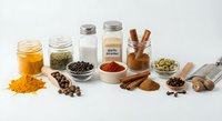 Assorted cooking spices and seasonings in glass jars and wooden spoons arranged on white background for culinary recipes and food preparation.