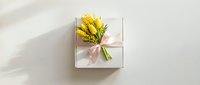 White gift box with yellow mimosa flowers and pink ribbon on neutral background for spring celebrations and International Women's Day greeting cards.