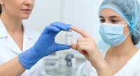 Female healthcare professionals in protective gear examining medical vial in clinical laboratory setting for pharmaceutical research and development.