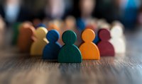 Colorful wooden figures representing diverse team members stand in row on wooden surface, symbolizing unity, leadership and workplace diversity concept.