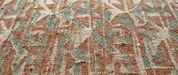 Vintage ornate carpet with intricate floral patterns in warm terracotta and sage green tones on textured woven fabric background for interior design projects.