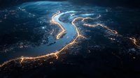 Aerial night view of illuminated river meandering through dark landscape with glowing city lights along shoreline creating luminous pattern from above.