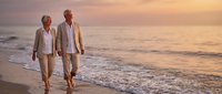 Senior couple walking hand in hand on beach at sunset enjoying romantic evening stroll by ocean waves in golden light for retirement lifestyle content.