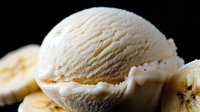 Creamy vanilla ice cream scoop with fresh banana slices on dark background, macro shot showing smooth texture and natural ingredients for dessert presentation.