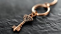 Elegant copper key charm on keyring resting on dark textured surface, antique style decorative metalwork for jewelry making and craft projects.