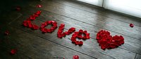 Red rose petals arranged to spell Love with a heart shape on a dark wooden floor, creating a romantic Valentine's Day decoration.