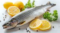 Fresh raw salmon trout with lemon slices, parsley herbs and peppercorns on white background, healthy cooking ingredients for seafood dish.