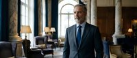 Confident mature businessman in elegant suit standing in luxurious hotel lobby with marble columns and classic interior design for corporate presentations.