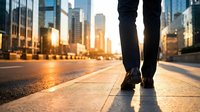 Business person walking on urban street at sunset with city skyline and golden hour lighting creating professional atmosphere for corporate concepts.