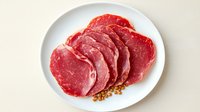 Fresh raw beef ribeye steaks sliced on white plate with mustard seeds, ready for cooking gourmet meal.