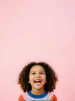 Young child with curly brown hair and mixed ethnicity, wearing colorful striped sweater, laughing joyfully against pink background. Studio portrait for advertising, parenting, education, and lifestyle design projects.