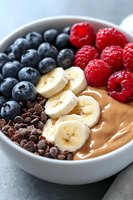 Creamy smoothie bowl topped with fresh blueberries, raspberries, sliced bananas and chocolate chips in white ceramic bowl, healthy breakfast concept.
