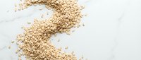Scattered oat flakes and cereal grains on white marble surface, suitable for food photography, healthy breakfast, nutrition, and culinary content.