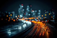 Blurred city highway at night with colorful bokeh lights from traffic and urban buildings creating atmospheric depth and motion blur effect.