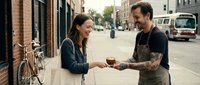 Male barista with tattoos serving coffee to female customer on urban street, small business owner interaction, local cafe commerce and community engagement.