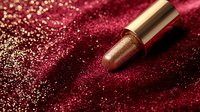 Luxurious golden lipstick on dark red glitter background with bokeh effect and metallic shimmer. Glamorous cosmetic product photography for beauty and makeup.