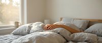 Cozy bedroom with unmade bed, soft linen bedding, wooden headboard, and warm sunlight streaming through window for home decor and lifestyle content.