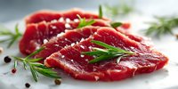 Fresh raw beef steak with rosemary, salt, and peppercorns on white surface, ready for cooking.