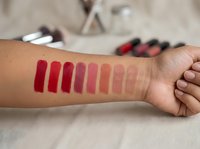 Lipstick color swatches on woman's arm showing red to nude gradient shades for makeup testing and beauty product selection.