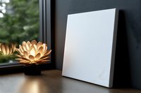 Blank white canvas mockup on wooden table with glowing lotus lamp decoration near window, creating cozy atmosphere with natural light and shadows.