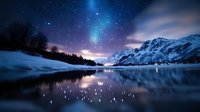 Aurora borealis dancing over snow-covered mountains and frozen lake with starry night sky reflecting in calm water creating magical winter landscape.