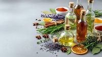 Essential oils in glass bottles with lavender, herbs, spices and dried citrus on gray background for aromatherapy and natural wellness treatments.