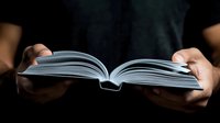 Female hands holding open book with white pages against dark background, dramatic lighting creates atmospheric mood for reading, education and literature concepts.