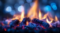 Burning wood embers and orange flames with blue bokeh background create atmospheric mood. Macro shot of glowing coals and fire shows warmth and comfort.