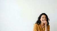 Young woman with dark hair and medium skin tone wearing mustard yellow shirt, smiling while eating sandwich against white background for food, lifestyle and casual dining concepts.