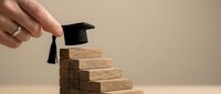 Hand placing graduation cap on wooden block steps representing educational achievement and academic success journey.