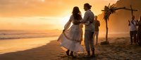 Romantic couple dancing on beach at sunset during tropical wedding ceremony with floral arch and ocean waves in background creating intimate celebration moment.