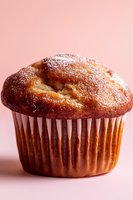 Fresh baked vanilla muffin with powdered sugar dusting on top against pink background, close-up view showing soft texture and golden brown color.