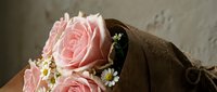 Delicate pink roses with small white flowers wrapped in brown kraft paper against neutral background for romantic gifts and floral arrangements.