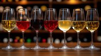 Wine glasses filled with different varieties showing red, white and rose wines lined up on dark wooden bar counter with soft bokeh background lighting.