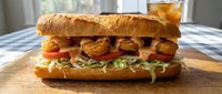 Crispy fried shrimp po boy sandwich with lettuce and tomato on crusty French bread served on wooden cutting board for restaurant menu photography.