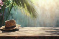 Straw hat on wooden table with palm leaves and soft sunlight creating tropical summer atmosphere, selective focus on rustic background.