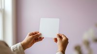 Hands holding blank white card against soft purple background with natural light, suitable for mockups, branding, and promotional designs.