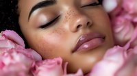 Young African American woman with freckles and glossy lips sleeping peacefully among pink rose petals, representing natural beauty, wellness and skincare.