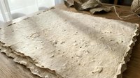 Handmade paper sheets with natural texture and deckled edges stacked on wooden surface for craft projects and artistic applications.