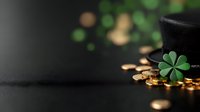 Magical St Patrick's Day composition with leprechaun black hat, golden coins and green clover on dark background with bokeh lights and copy space.