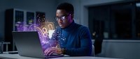 Young African American man working on laptop with glowing digital interface hologram in modern office environment at night for technology concepts.