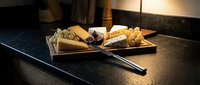 Assorted cheese and crackers arranged on wooden serving board with chopsticks on dark countertop, appetizer spread for entertaining and dining occasions.