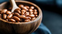 Fresh roasted coffee beans in wooden bowl with scoop on dark background, macro shot with selective focus and shallow depth of field for food photography.