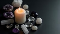 Burning candle surrounded by healing crystals and gemstones creating peaceful meditation atmosphere for spiritual wellness and relaxation practices.