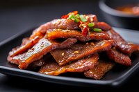 Glazed pork ribs with sweet and savory sauce garnished with fresh scallions on black plate. Asian cuisine barbecue dish for restaurant menu and food photography.