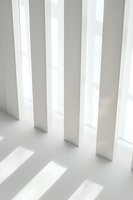 Minimalist white architectural detail with parallel vertical columns casting dramatic diagonal shadows on light surface, creating geometric pattern.