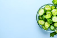 Fresh sliced cucumber in glass bowl on light blue background with copy space. Clean eating and healthy food concept for social media and blogs.