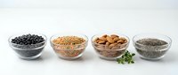 Healthy superfood collection in glass bowls featuring black beans, quinoa, almonds and chia seeds arranged on white background for nutrition concepts.