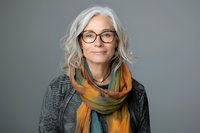 Elegant mature woman with silver hair wearing stylish glasses and colorful scarf against gray background, natural beauty portrait showcasing aging gracefully.