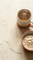 Overhead view of steaming herbal tea in ceramic mug and sliced almonds in terracotta bowl on neutral textured surface, ideal for wellness and breakfast content.